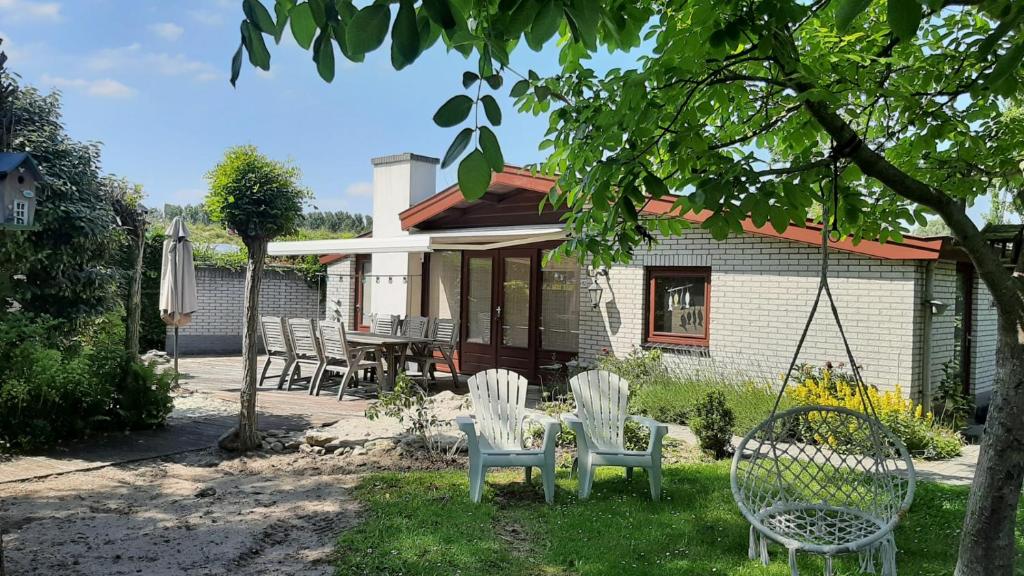 a yard with chairs and a swing in front of a house at Bungalow de Pluumpot in Scherpenisse