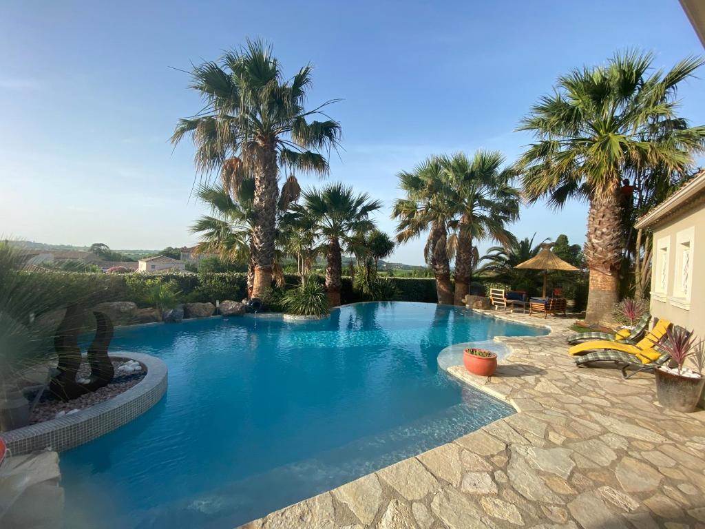 una gran piscina con palmeras en un patio en KABEN Superbe villa 4 étoiles, piscine chauffée, sauna, jacuzzi, pétanque, sans vis à vis en Saint-Geniès-de-Fontedit