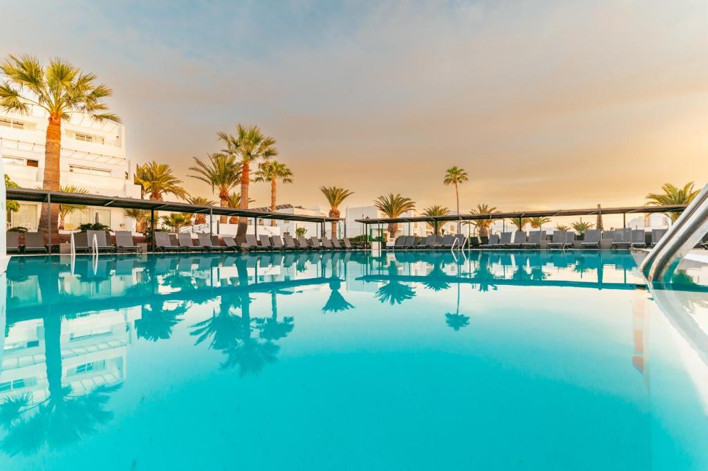 a swimming pool with palm trees and a building at Aequora Lanzarote Suites in Puerto del Carmen