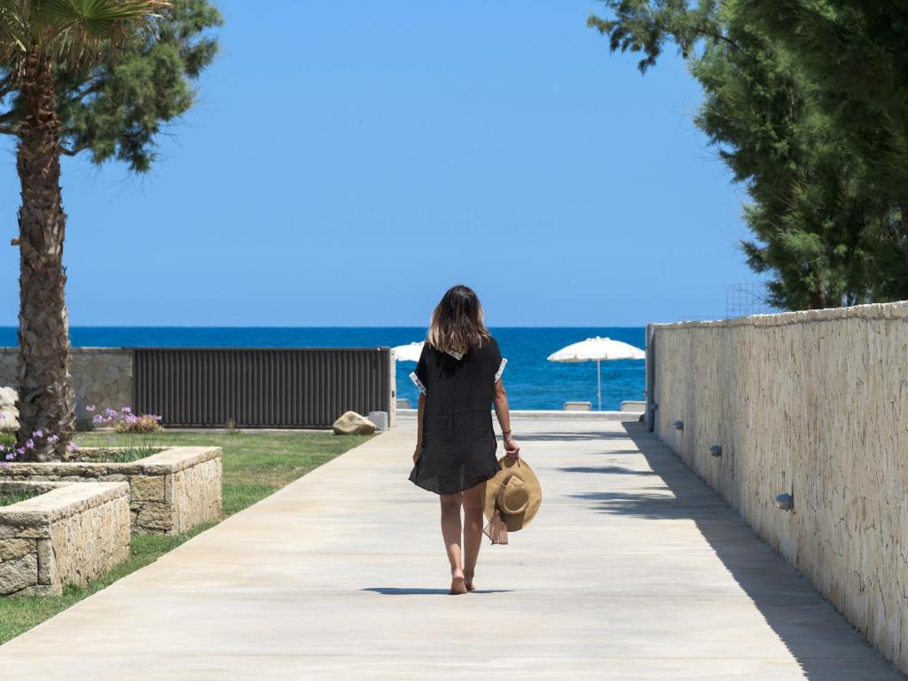 una mujer caminando por una acera cerca de la playa en Amalthia Villa, an Evanescence Retreat, By ThinkVilla en Tavronitis