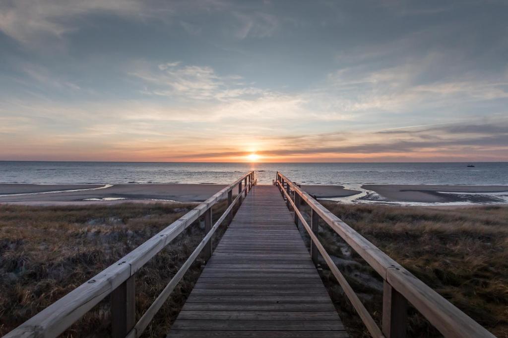 einen Holzsteg zum Strand bei Sonnenuntergang in der Unterkunft Marin Hotel Sylt in Westerland