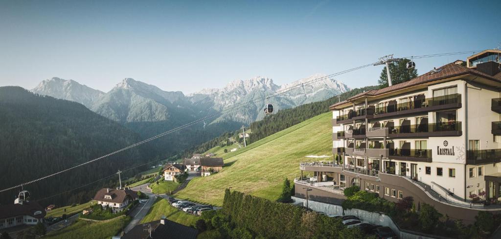 a building on a hill with mountains in the background at Kronplatz-Resort Hotel Kristall in Valdaora