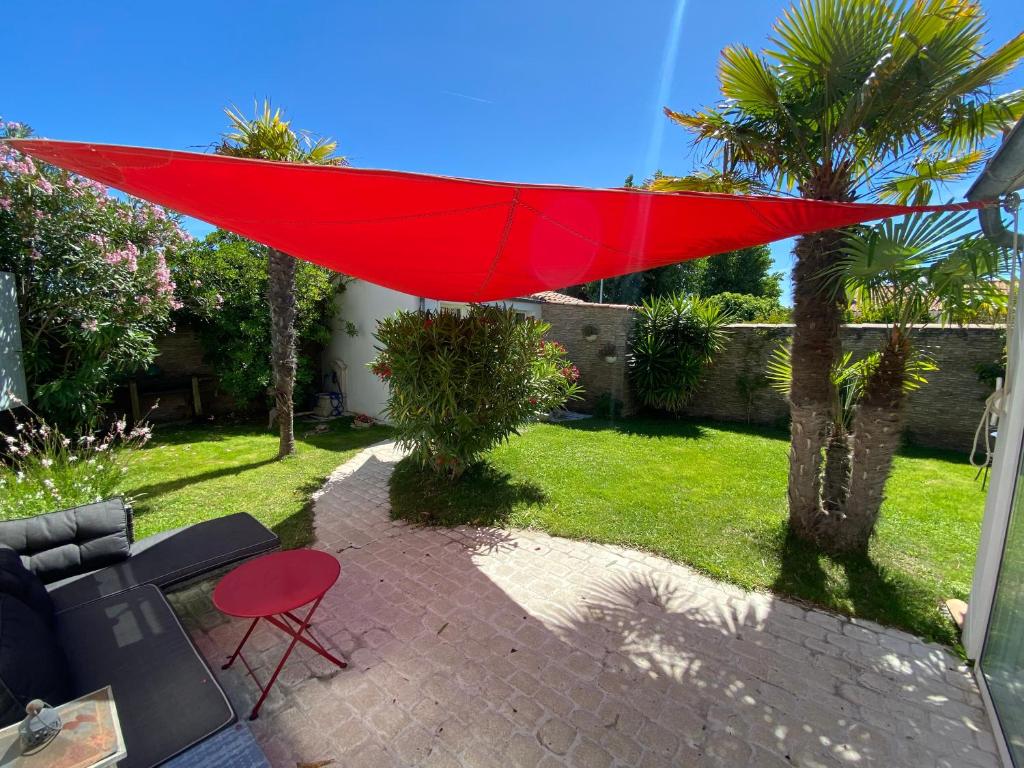 een rode parasol boven een patio met een tafel en een stoel bij ORIANE Jolie maison proche plage in Le Bois-Plage-en-Ré