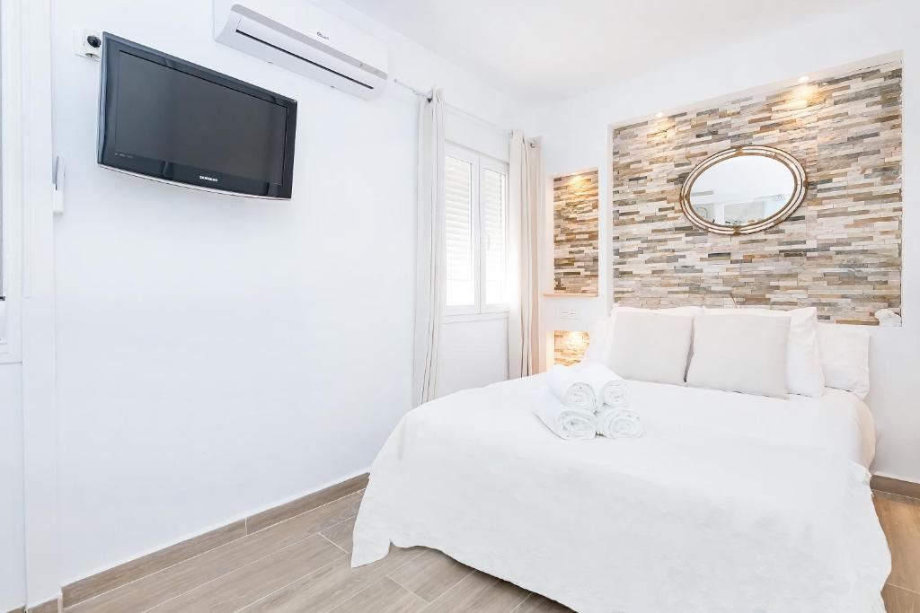 a bedroom with a white bed and a tv on a wall at Marmoles 21, City Center Apartment in Málaga