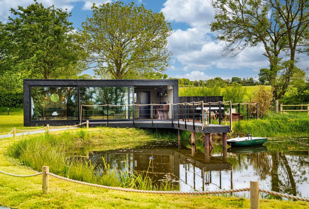 a glass house on a lake with a dock at Rusty Boathouse in Llanarth