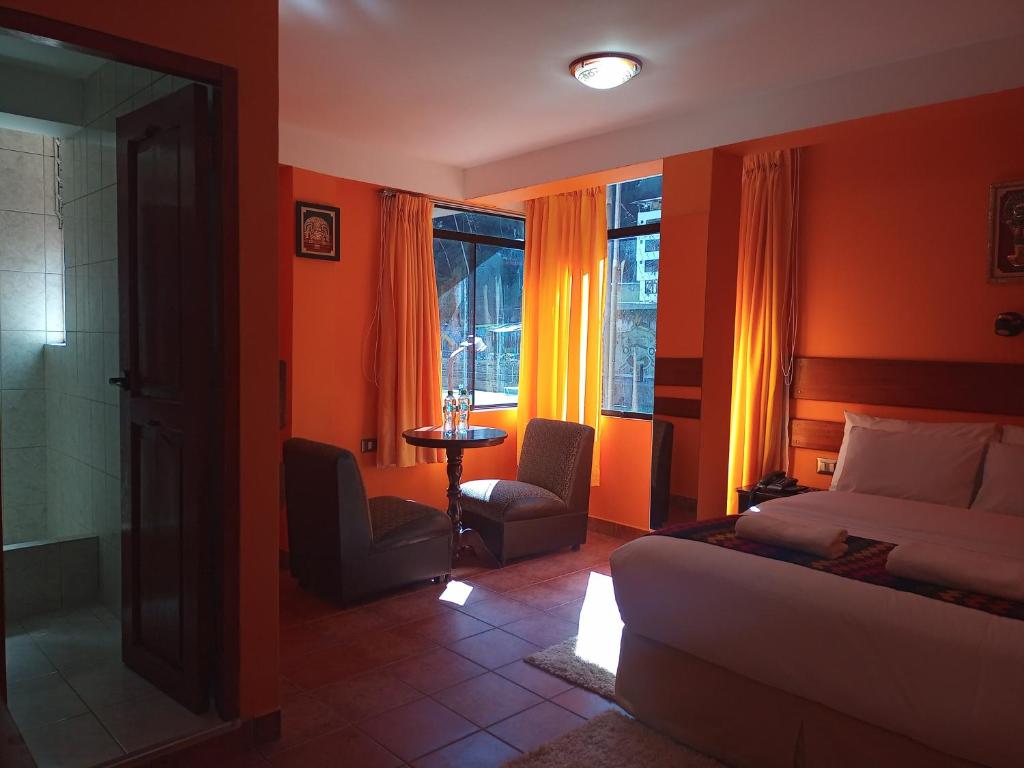 1 dormitorio con paredes de color naranja, 1 cama y 1 mesa en Hotel Rio Dorado MachuPicchu en Machu Picchu