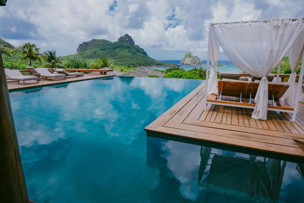 a pool at a resort with chairs and the ocean at Pousada Maravilha in Fernando de Noronha