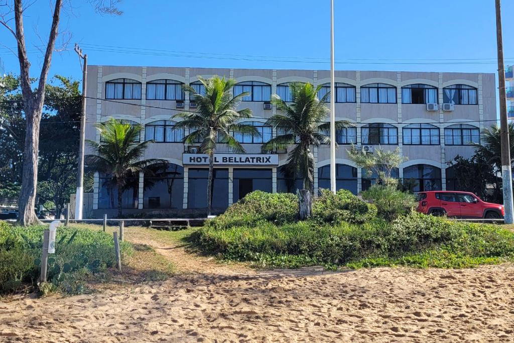 a building on the beach with palm trees in front at Hotel Bellatrix in Macaé