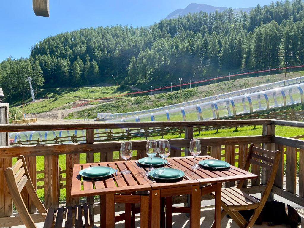 een houten tafel met borden en wijnglazen op een balkon bij Appartement 2 chambres vue pistes, parking privatif in Les Orres