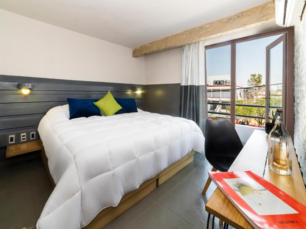Hotel NEXT في غواذالاخارا: غرفة نوم مع سرير أبيض كبير ومكتب