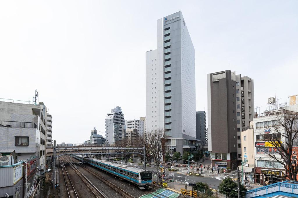 een trein op rails in een stad met gebouwen bij Via Inn Shinagawa Oimachi in Tokyo