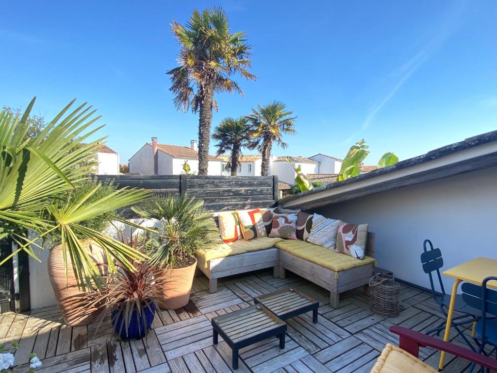 a patio with a couch and palm trees on a roof at La Terrasse du Bois Plage in Le Bois-Plage-en-Ré