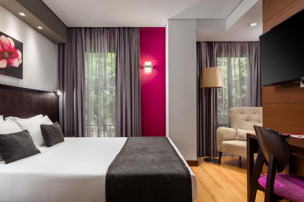 A double room with a separate desk corner, armchair and curtained window.