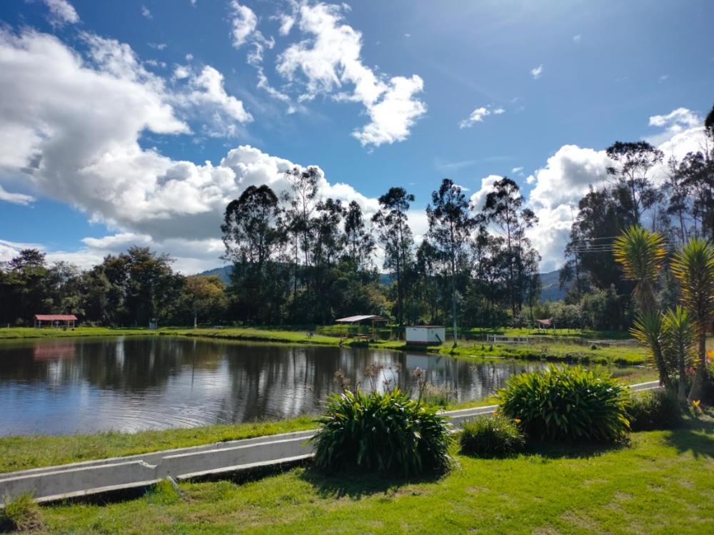 a pond in the middle of a park with clouds in the sky at Naturaleza Muisca in Guasca
