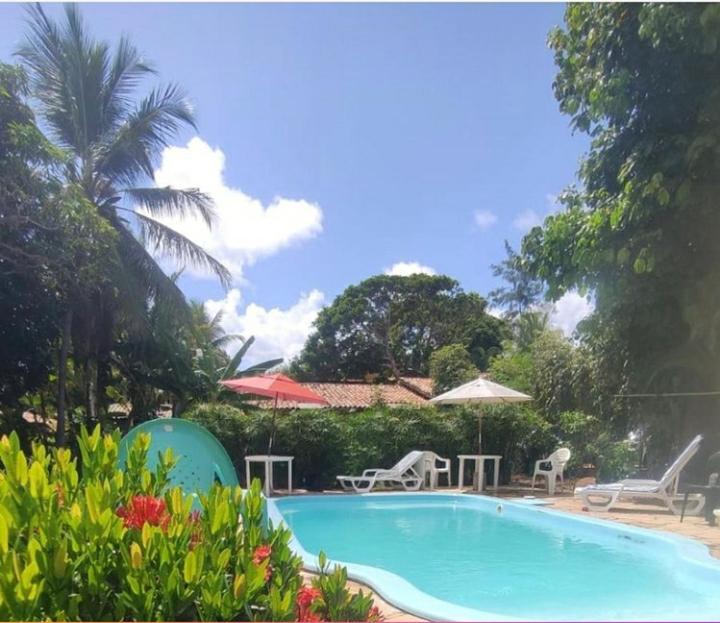 a swimming pool with chairs and umbrellas in a yard at Pousada restaurante Vila Imbassai in Imbassai