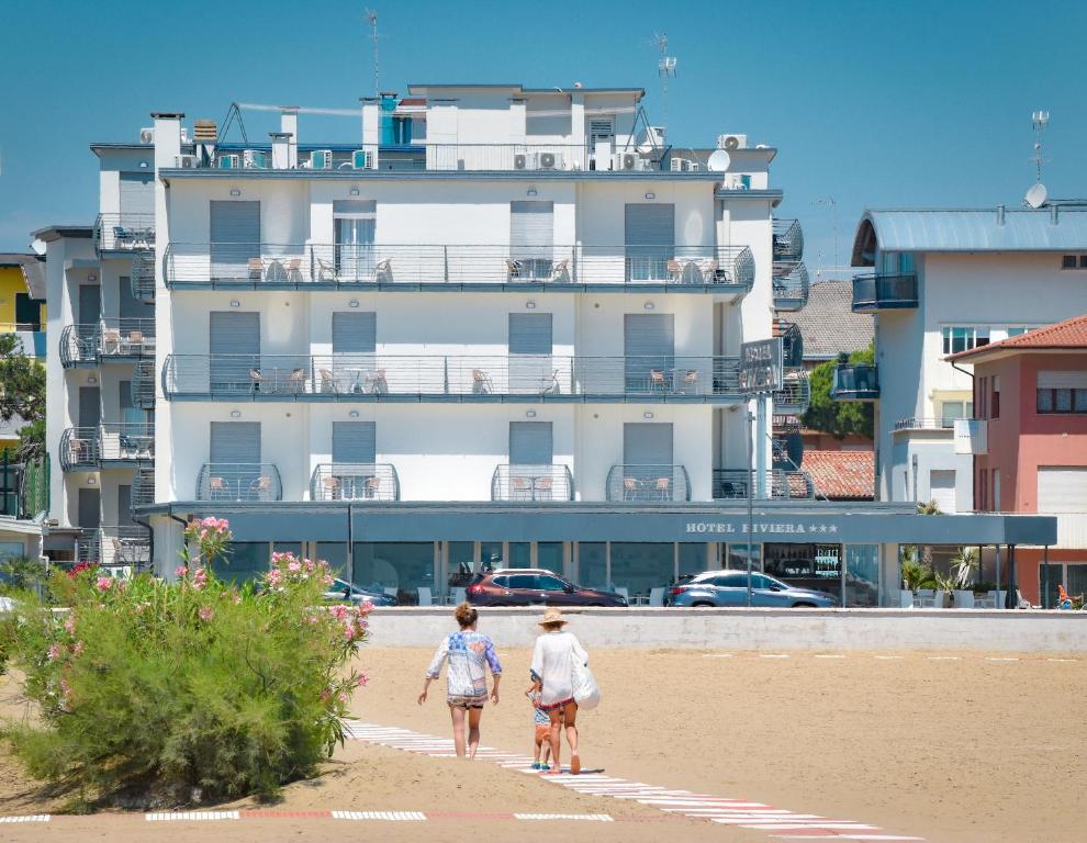 two women walking on the beach in front of a building at Hotel Riviera in Caorle