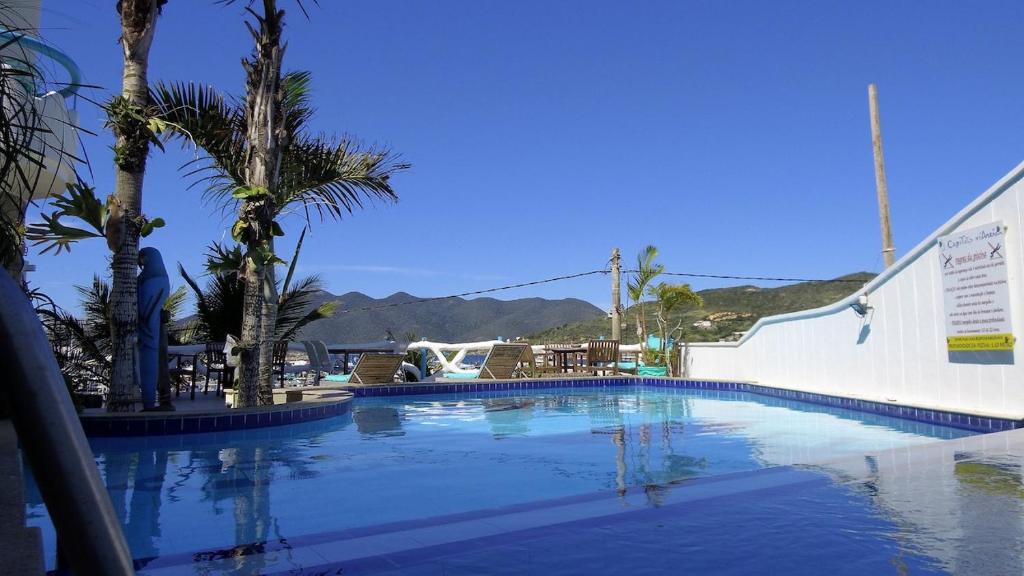 a swimming pool with palm trees and mountains in the background at Capitão N Areia Pousada in Arraial do Cabo