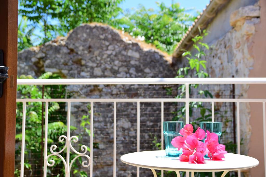 a table with two glasses and pink flowers on it at Fiori Studios Fiscardo in Fiskardho