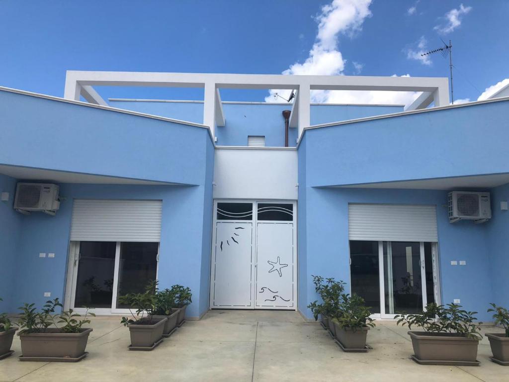um edifício azul com uma porta branca e vasos de plantas em Torrepali appartamenti em Torre Pali
