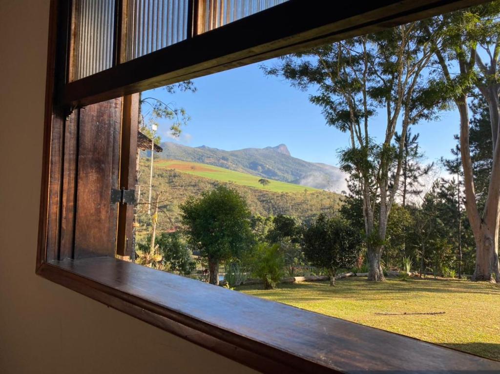 a window with a view of a field and mountains at Pousada Lenda da Montanha in Aiuruoca