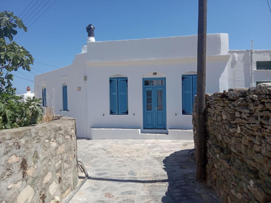 a white building with blue doors and a stone wall at Kafenes house Αναπαλαιώμενο παραδοσιακό σπίτι in Artemonas