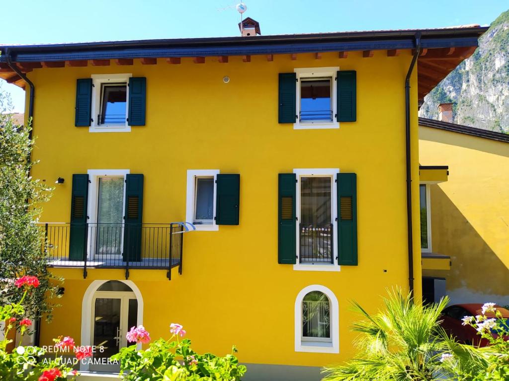 a yellow house with green shutters and flowers at Appartamento Carta da Zucchero in Riva del Garda