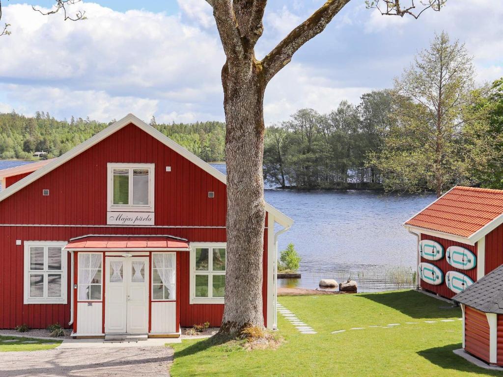 ein rotes Gebäude mit einem Baum vor einem See in der Unterkunft Holiday home UNNARYD IV in Unnaryd