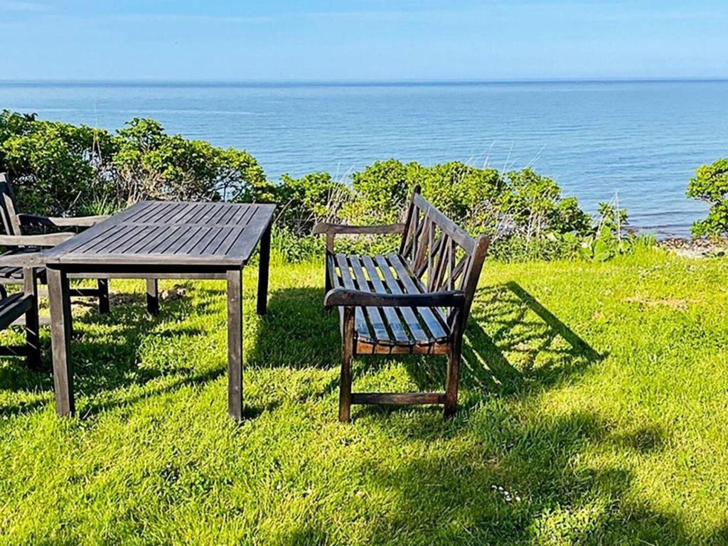 a wooden table and bench sitting next to the ocean at Seaside Serenity in LumsAYs-By Traum in Ebbeløkke
