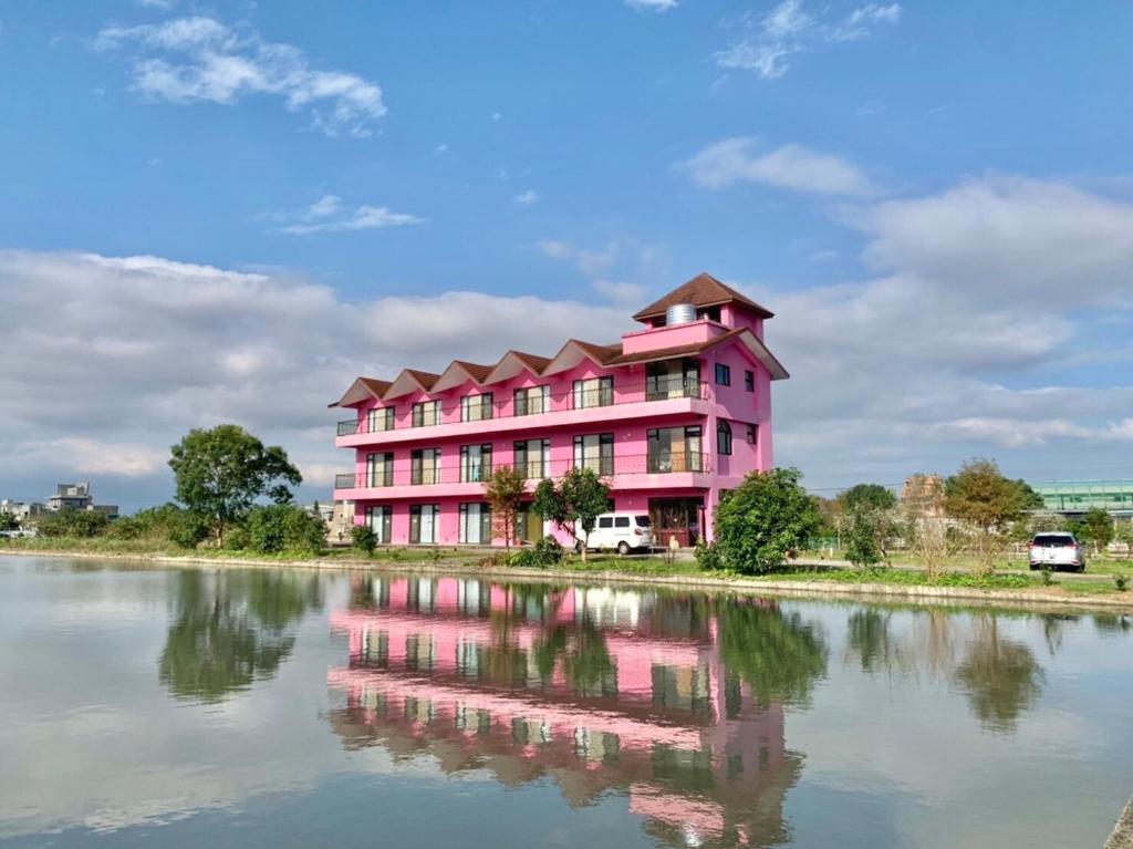 un edificio rosa junto a un cuerpo de agua en Fairy Story Village Farm B&B, en Dongshan