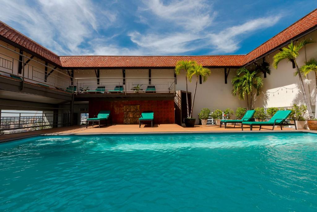 a swimming pool in front of a building with blue chairs at Pinnacle Lumpinee Park Hotel in Bangkok