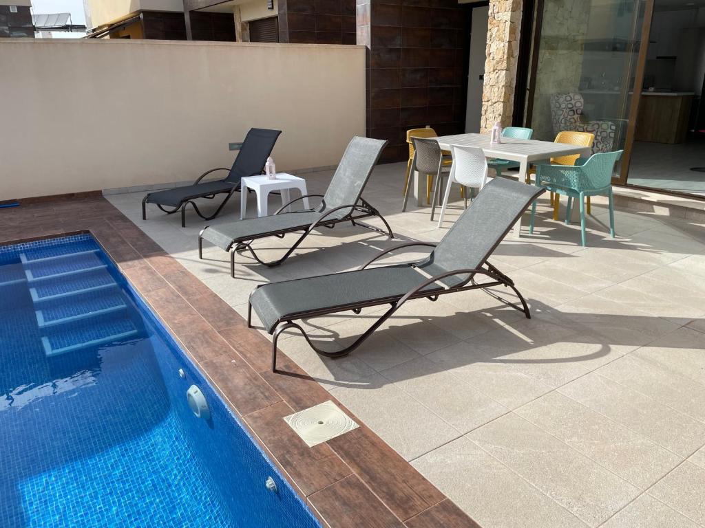 eine Gruppe Stühle und ein Tisch neben einem Pool in der Unterkunft Villa de 2022 moderna y con piscina privada in San Pedro del Pinatar