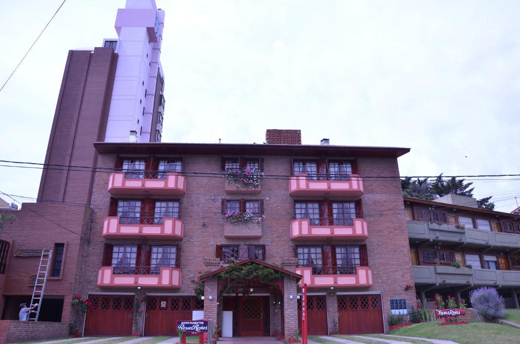 ein rotes Backsteingebäude mit Blumen auf der Vorderseite in der Unterkunft Departamentos Familiares Rosas Rojas in Villa Gesell