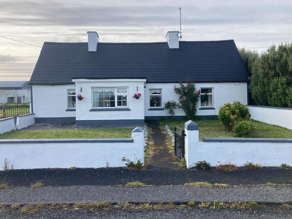 a white house with a black roof at Maisie's Seaside Cottage in Quilty