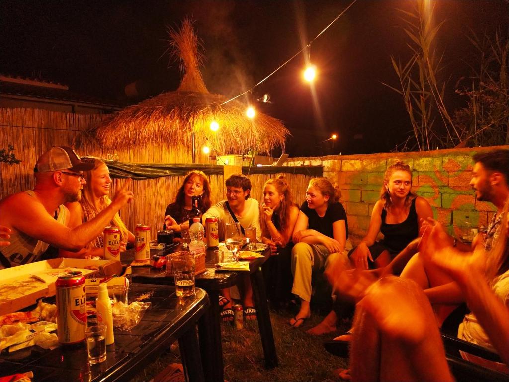 Pinegroove Hostel Vlora في فلوره: مجموعة من الناس يجلسون حول طاولة في الليل