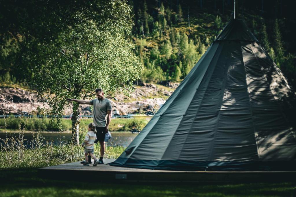 Ein Mann und ein Kind stehen neben einem Zelt in der Unterkunft Morgedal Lavvo Camping in Morgedal