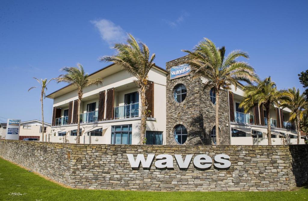 a building with palm trees behind a stone wall at Waves in Orewa