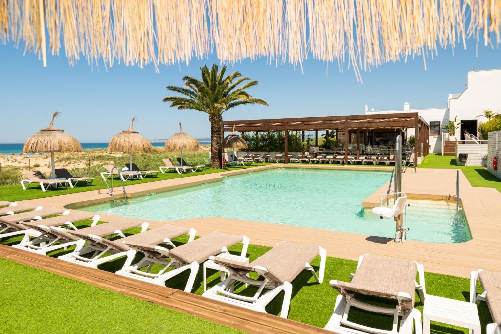 a pool with chaise lounges and chairs next to the ocean at Hotel Antonio in Zahara de los Atunes