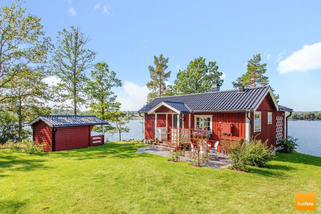 une cabine rouge sur une pelouse à côté d'une masse d'eau dans l'établissement Ekudden. Idylliskt nära sjö. Egen strand., à Rimforsa