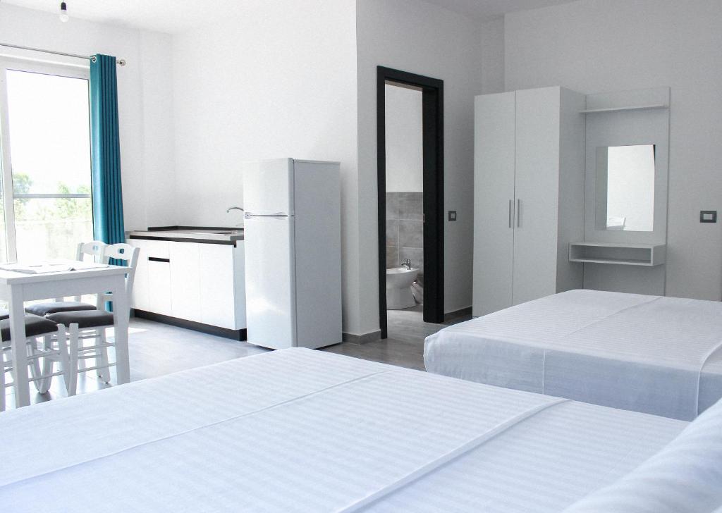 a white bedroom with two beds and a refrigerator at LUMNIK - Hotel & Apartments in Lezhë