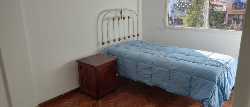 a bed with a blue blanket next to a window at DEPARTAMENTO CASEROS TRES Dormitorios in Salta