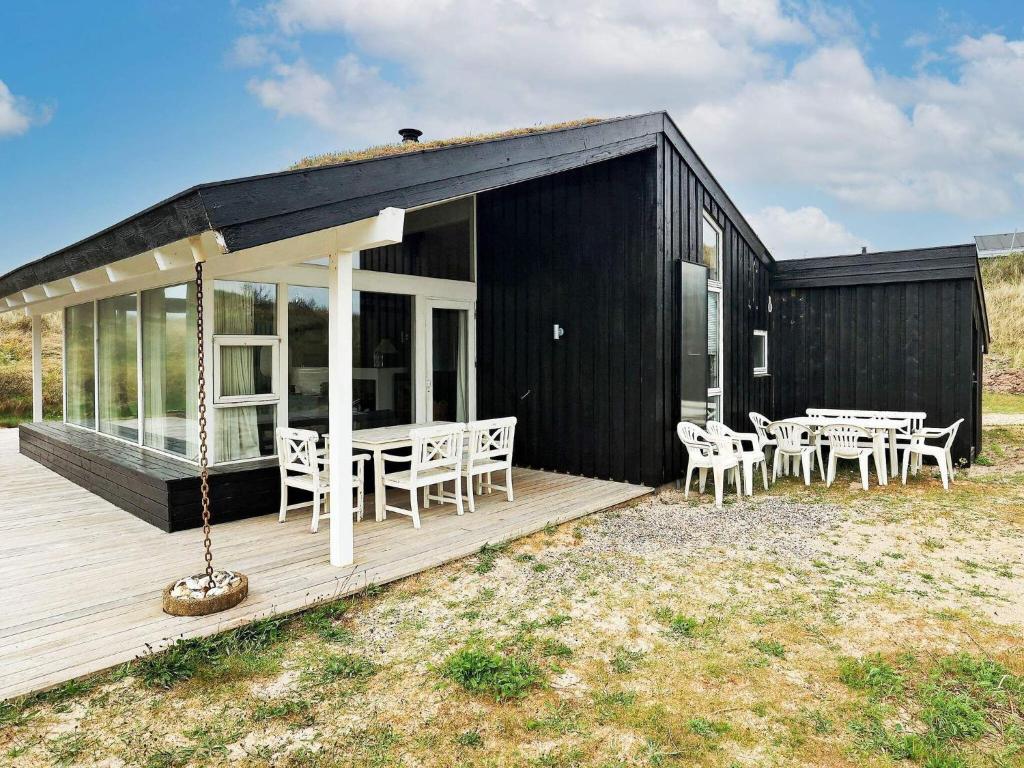 a black house with tables and chairs on a deck at 8 person holiday home in Pandrup in Blokhus