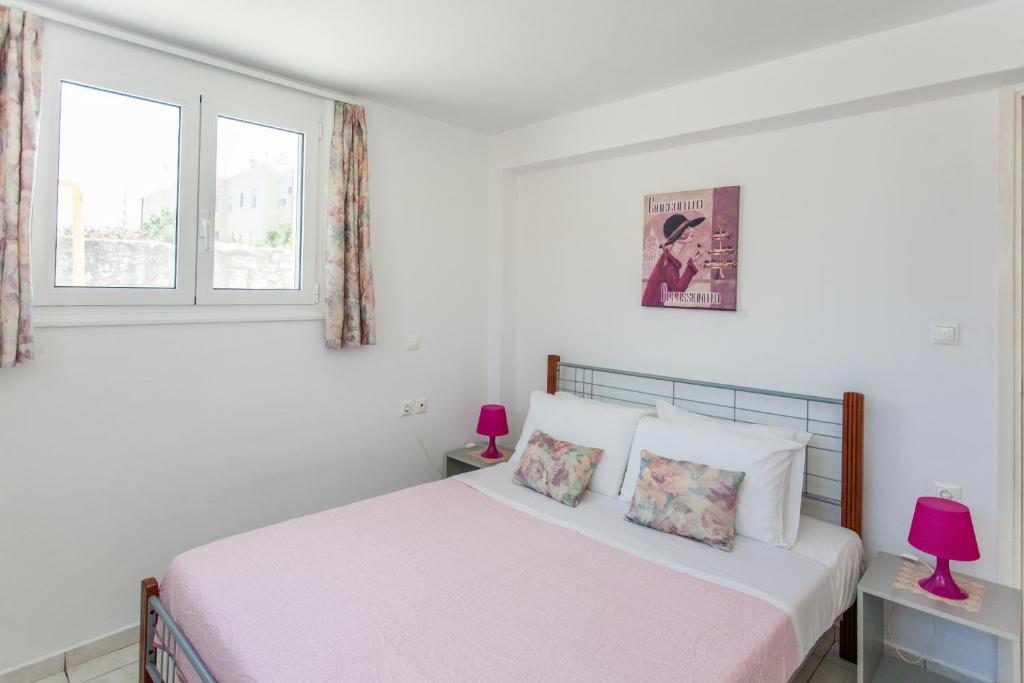 a white bedroom with a bed and two windows at Joy apartment by the sea in Rethymno
