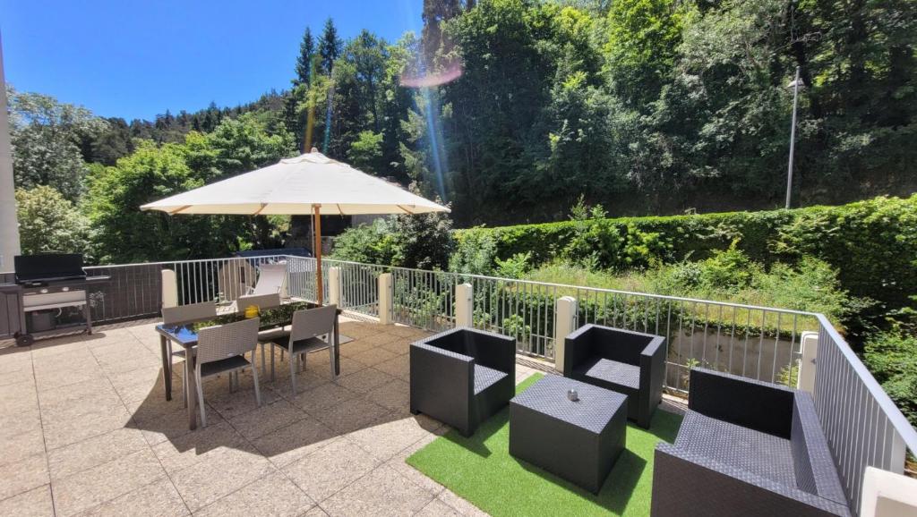 un patio con mesa, sillas y sombrilla en St Nectaire- Appartement Terrasse Privée- 4 personnes en Saint-Nectaire