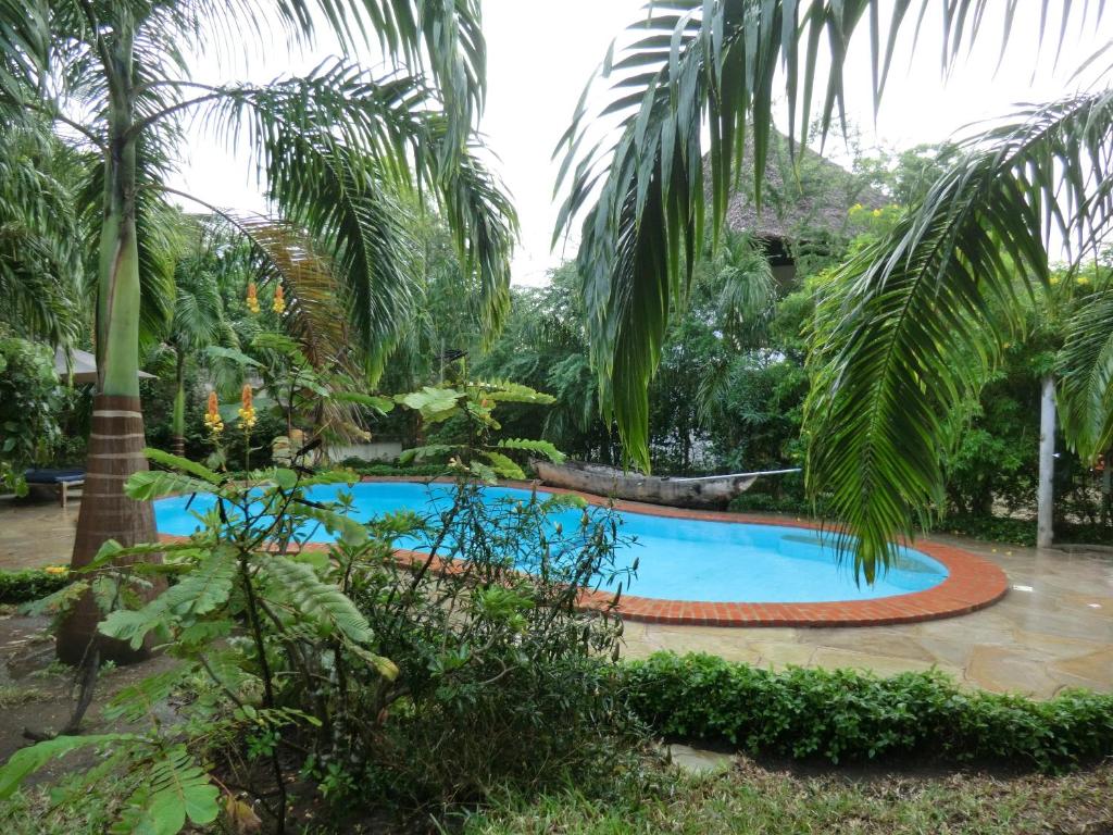 a swimming pool in a garden with palm trees at Villa Lamuhouse Diani Beach in Diani Beach