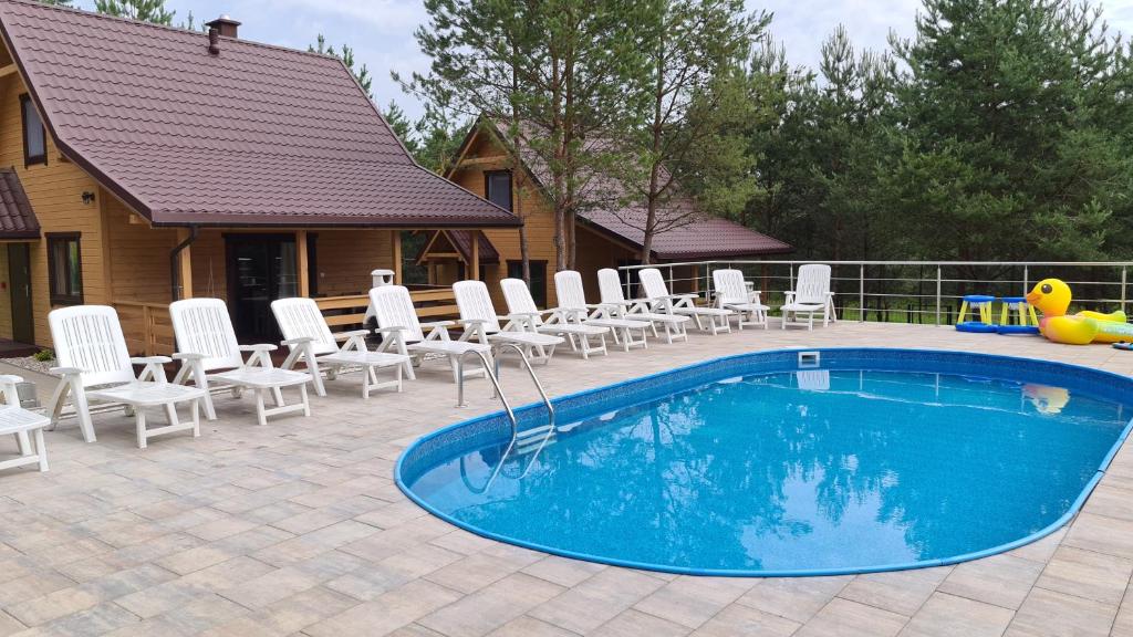 una piscina con sillas blancas y una casa en Sosnowe Wzgórze en Pasym