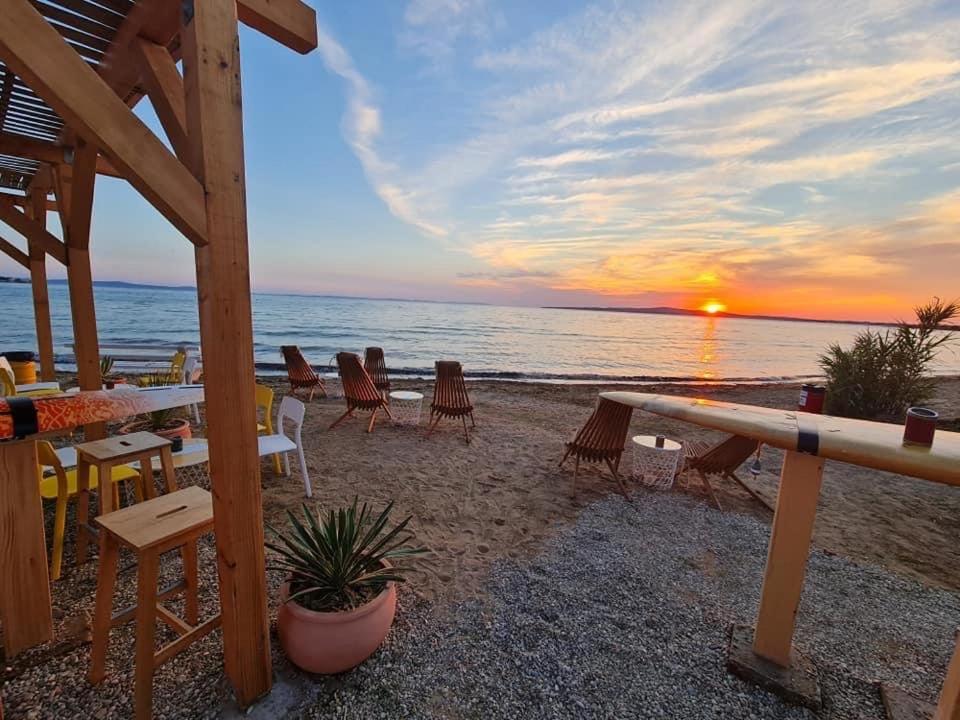 a sunset on the beach with tables and chairs at Apartments Lolo in Privlaka