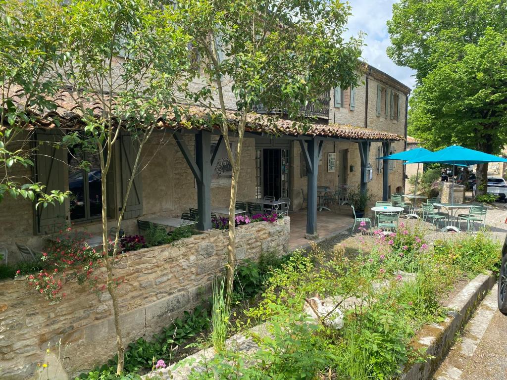 un edificio de piedra con un patio con mesas y sombrillas en L'étape du château, en Bruniquel