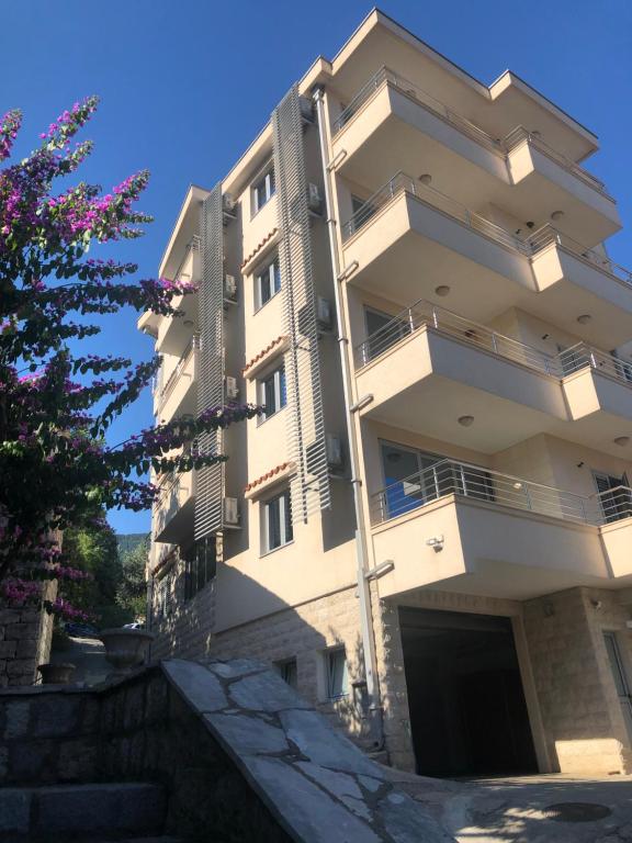 un edificio blanco alto con un árbol delante de él en Apartments Rafailović Ljubo, en Rafailovici