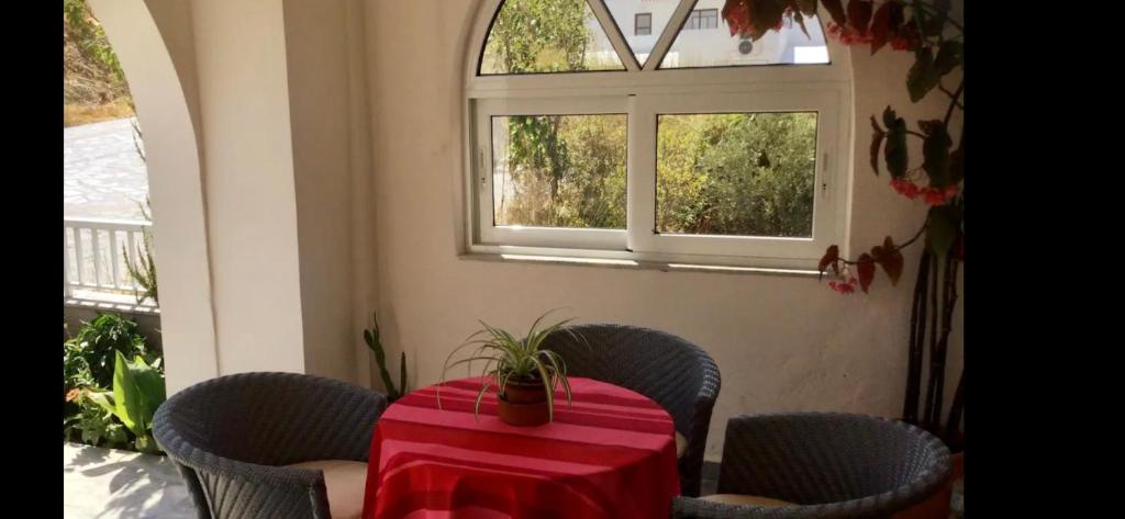 a table with a red table cloth and chairs and two windows at KOUMANS RESIDENCE AKOUMIA-TRIOPETRA in Akoumia