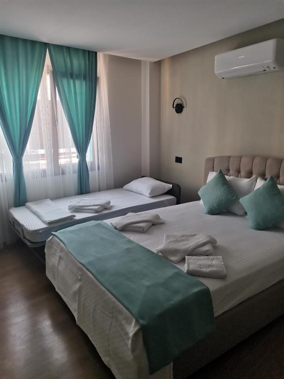 two beds in a hotel room with blue curtains at SIĞACIK SEN KONUK EVİ in Seferihisar